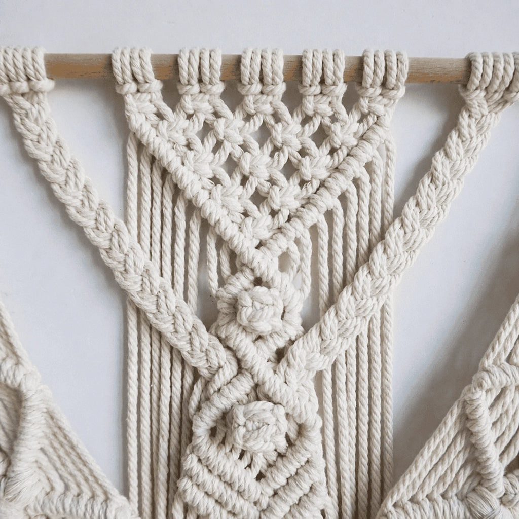 Macrame wall hanging on a textured white wall in a real home setting showing full piece and fringe detail