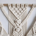 Macrame wall hanging on a textured white wall in a real home setting showing full piece and fringe detail